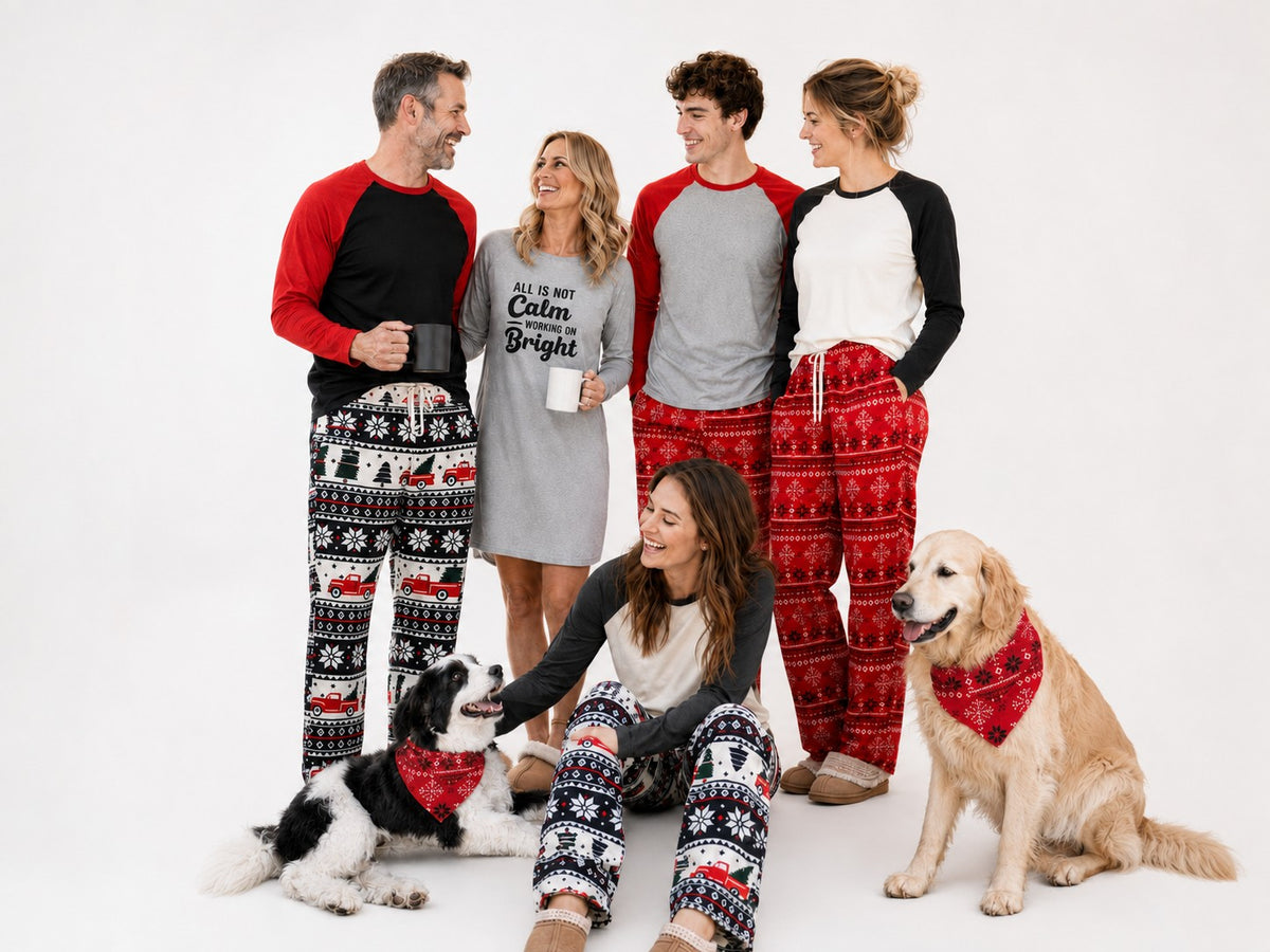 Adults mix and match holiday pajama separates with two dogs in coordinating bandanas.