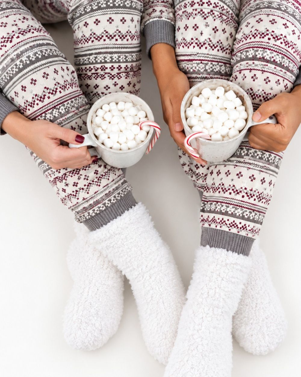 Two people in matching fair isle pajamas holding mugs of cocoa